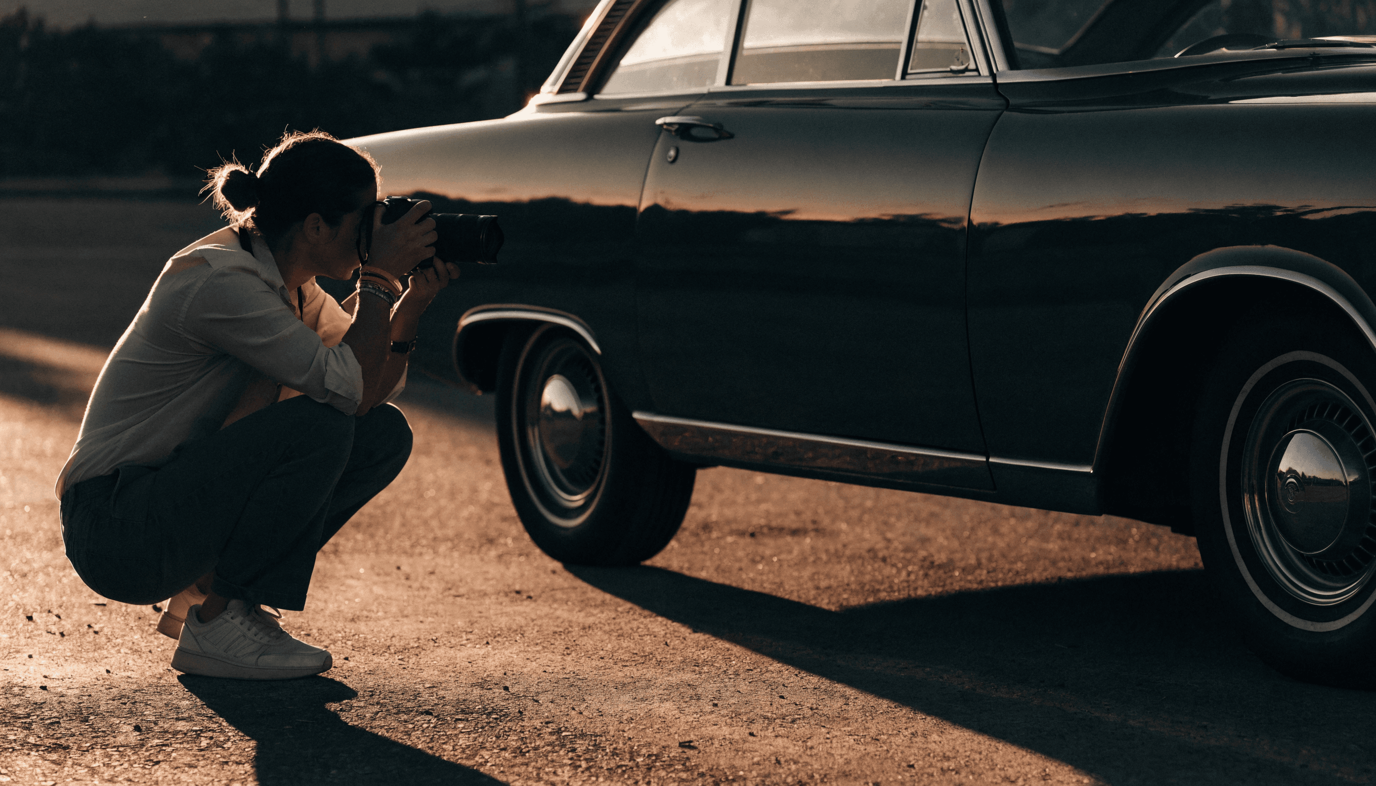 A photographer crouched low taking a photo of a classic car at golden hour