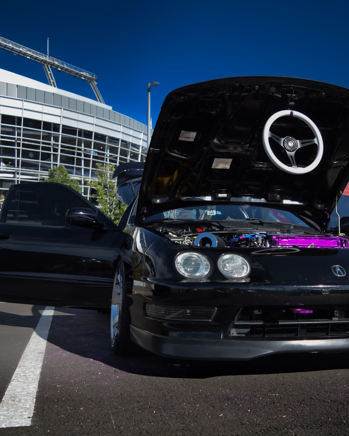 The Integra at a show with the hood up and the white RG steering wheel displayed on the engine