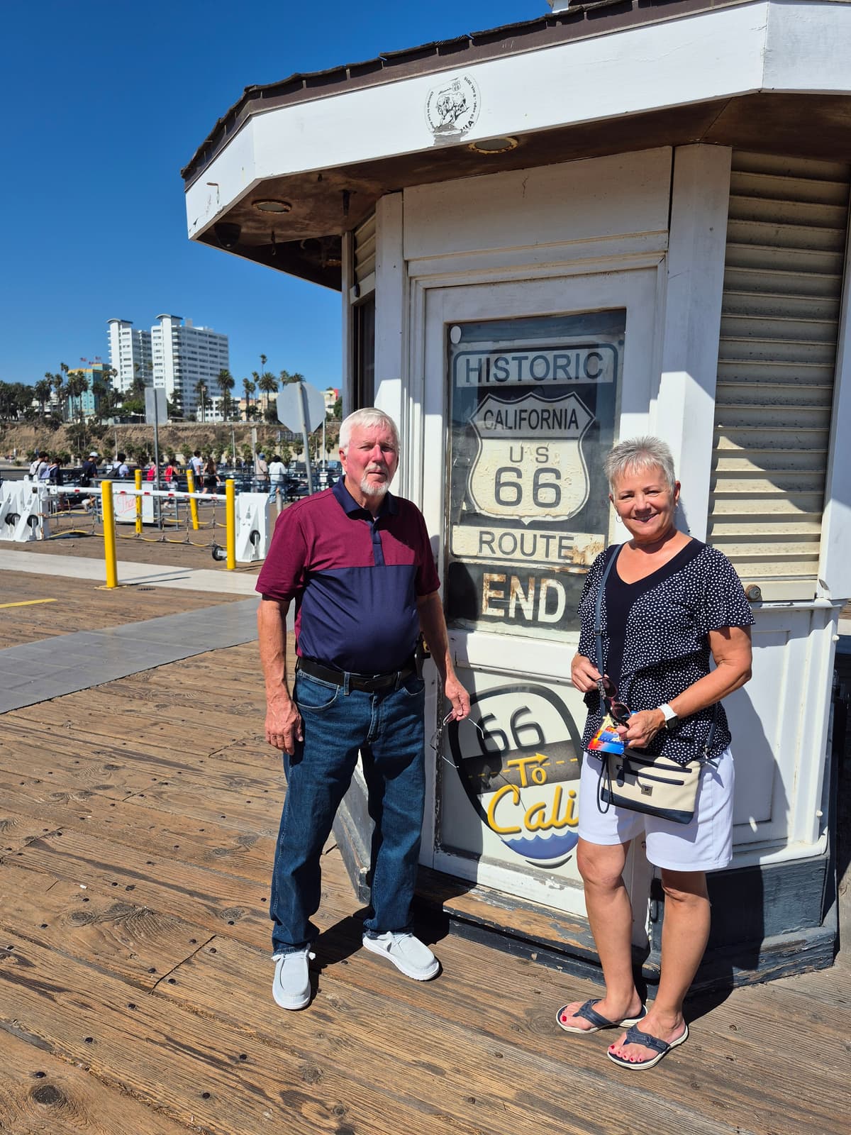A couple standing at the Route 66 End of the Trail sign on the Santa Monica Pier