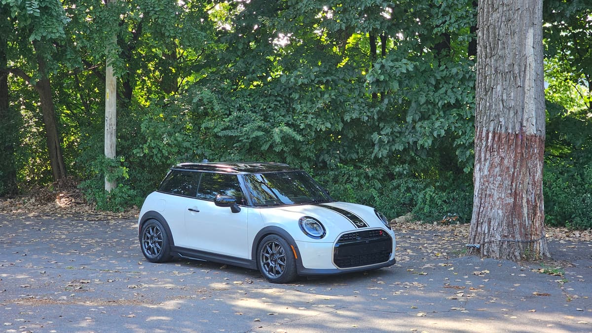 The Mini parked on gravel beside trees, showing the white paint and dark roof stripe