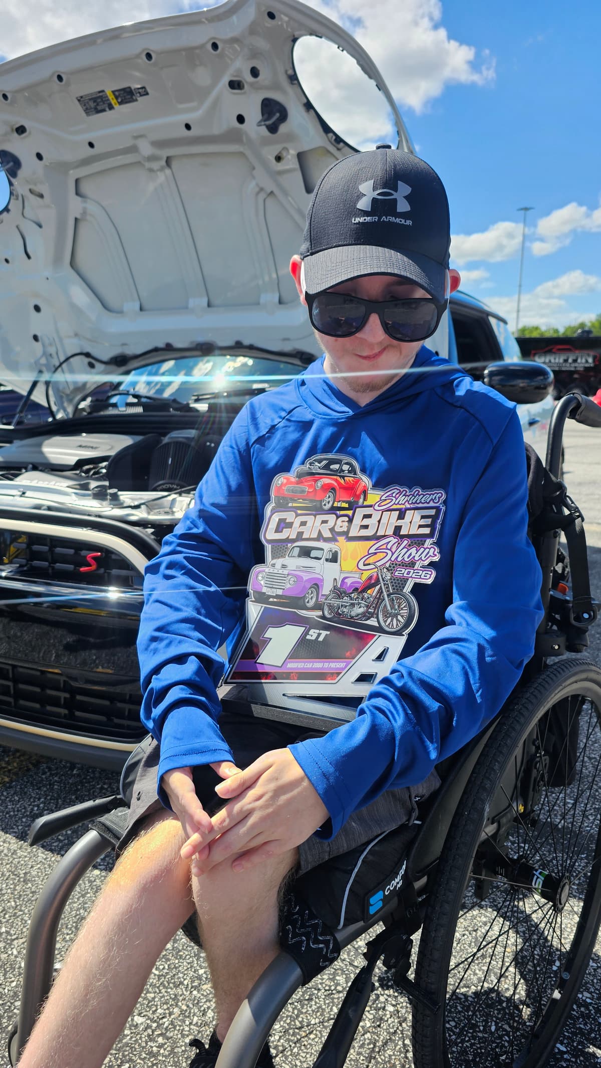 Steve's son in his wheelchair at a car show, in front of a car with the hood raised